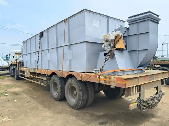 Large gray industrial baghouse filter unit loaded onto a flatbed semi-truck trailer for delivery