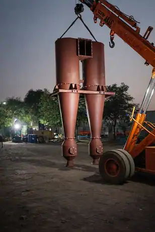 Reddish-brown dual cyclone particle separators being lifted by an industrial crane truck at dusk