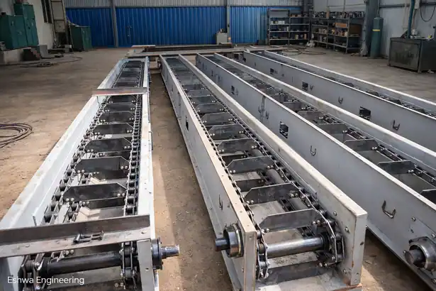 Internal look at a heavy-duty drag chain conveyor system showing the steel flight bars and chain links inside a workshop