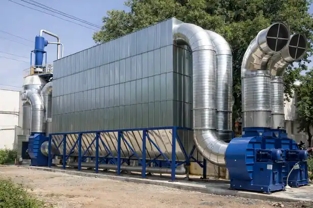 Outdoor industrial dust collection system with large filter housing, shiny stainless steel ducting, and blue heavy-duty blowers