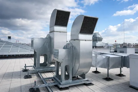 Twin roof-mounted commercial ventilation centrifugal fans with vertical discharge hoods on an outdoor platform