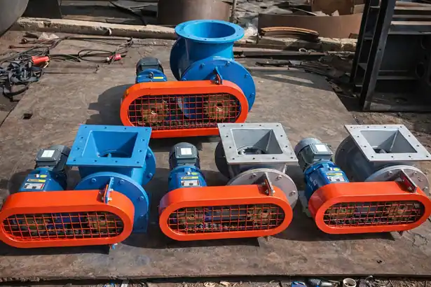 Group of manufactured blue rotary airlock valves with orange protective chain drive guards and electric motors on a workshop floor